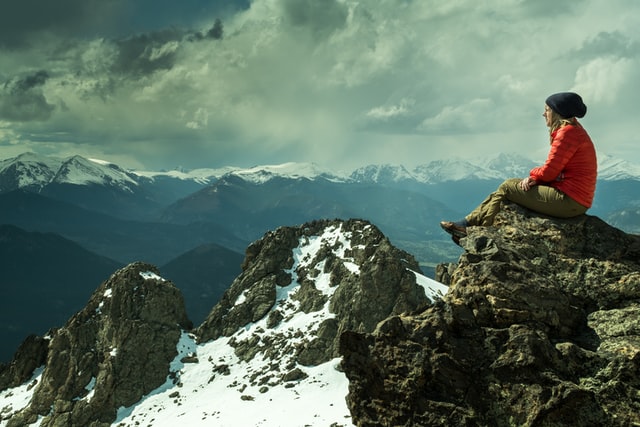 winter outdoor activities; a woman sitting on a mountain cliff reminiscing the winter view.