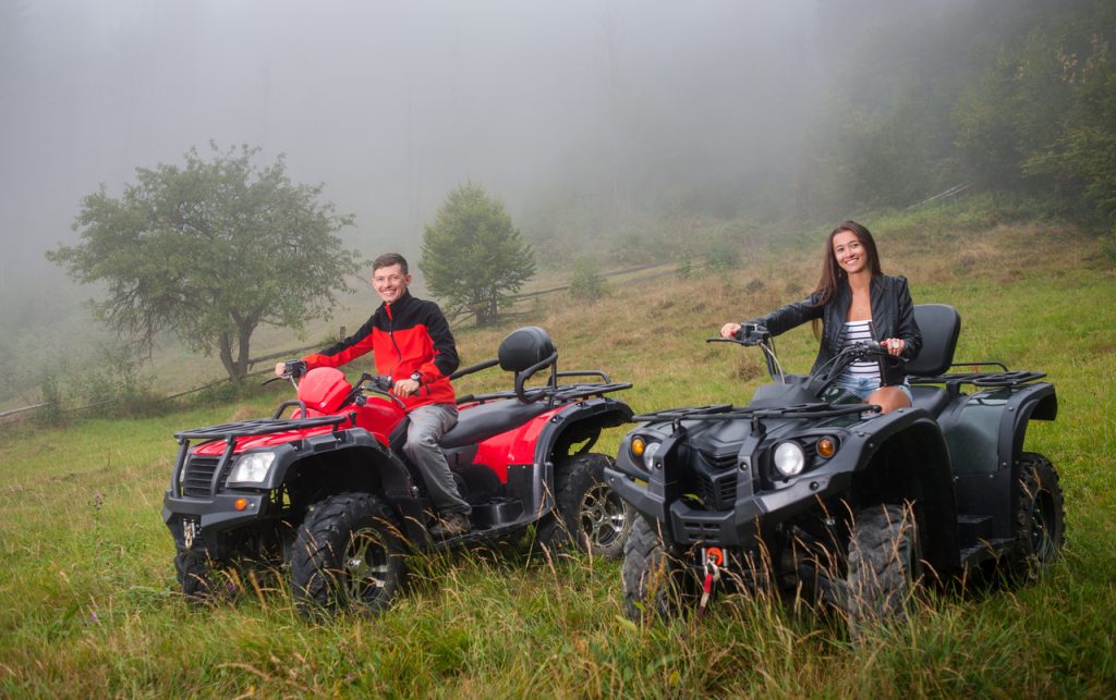 Happy couple driving four-wheeler ATV offroad. Smiling and looking at the camera