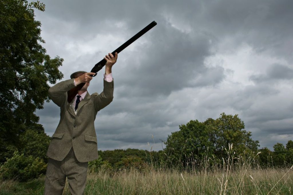 outdoor corporate activities, a young professional aiming a clay pigeon with a shotgun in an open setting