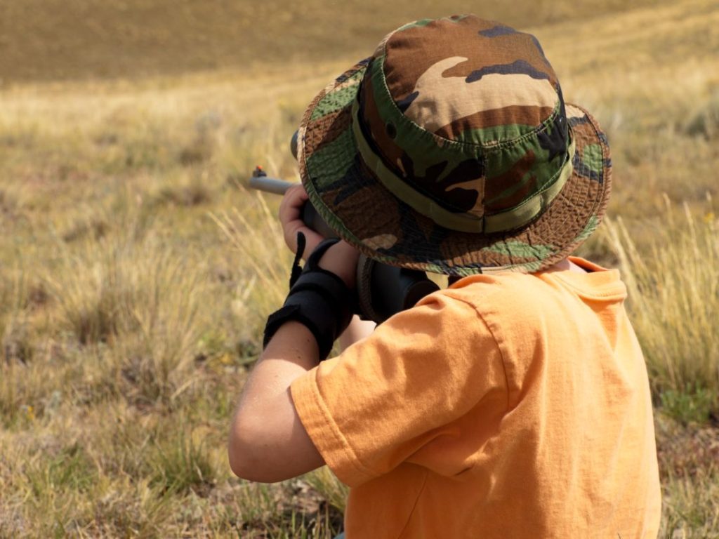 kids clay pigeon shooting safety, a child aiming a rifle on a clay pigeon
