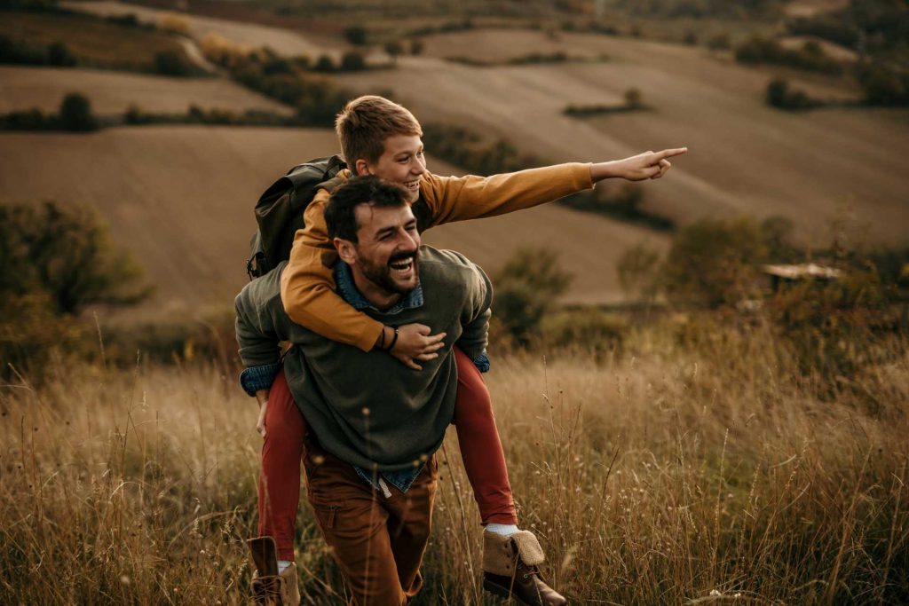 father son adventure, a father piggybacking his son across a field.