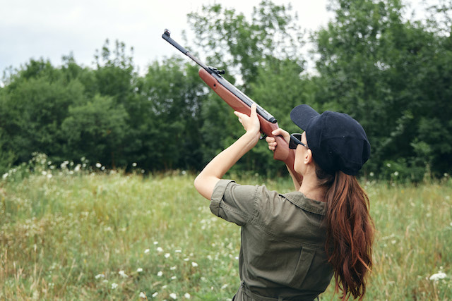 First time clay pigeon shooting, woman aiming with shotgun at target.